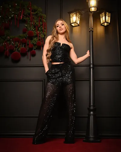 Editorial navideña de cuerpo entero: modelo con conjunto de lentejuelas negras apoyada en un farol vintage, sobre alfombra roja y panelería oscura